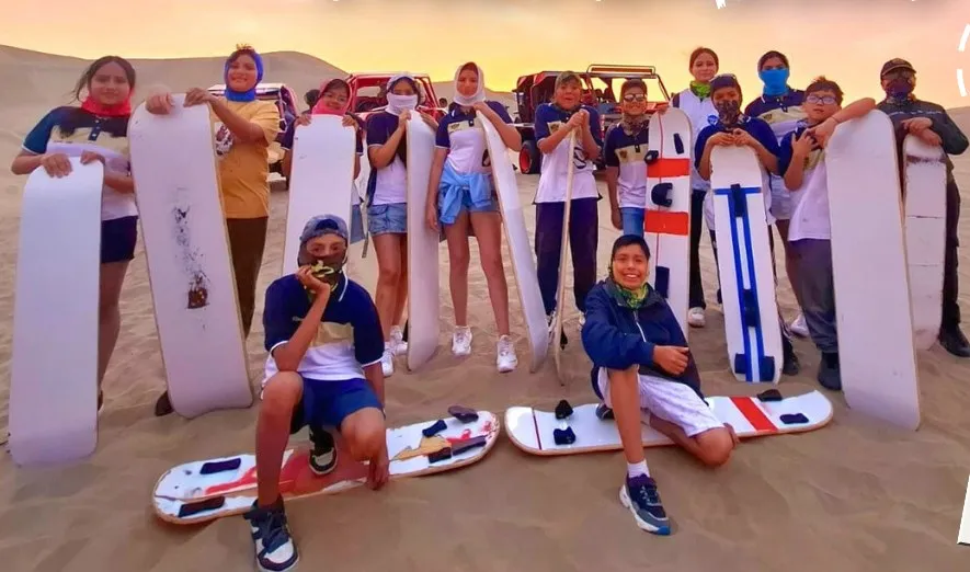 Promoción escolar con tablas de sandboard en las dunas de Huacachina al atardecer